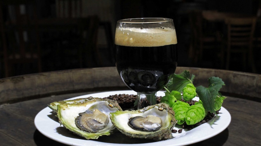 A glass of dark beer sitting on a plate surrounded by oysters.
