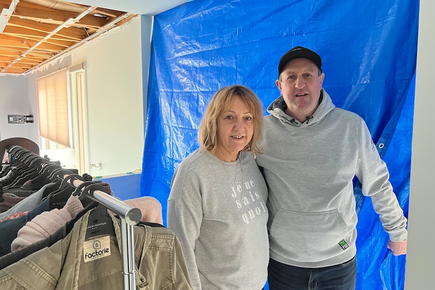 couple in grey jumpers stand together inside storm damaged home