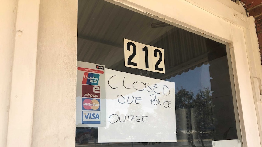 A glass door has a sign reading "Closed due to power outage"