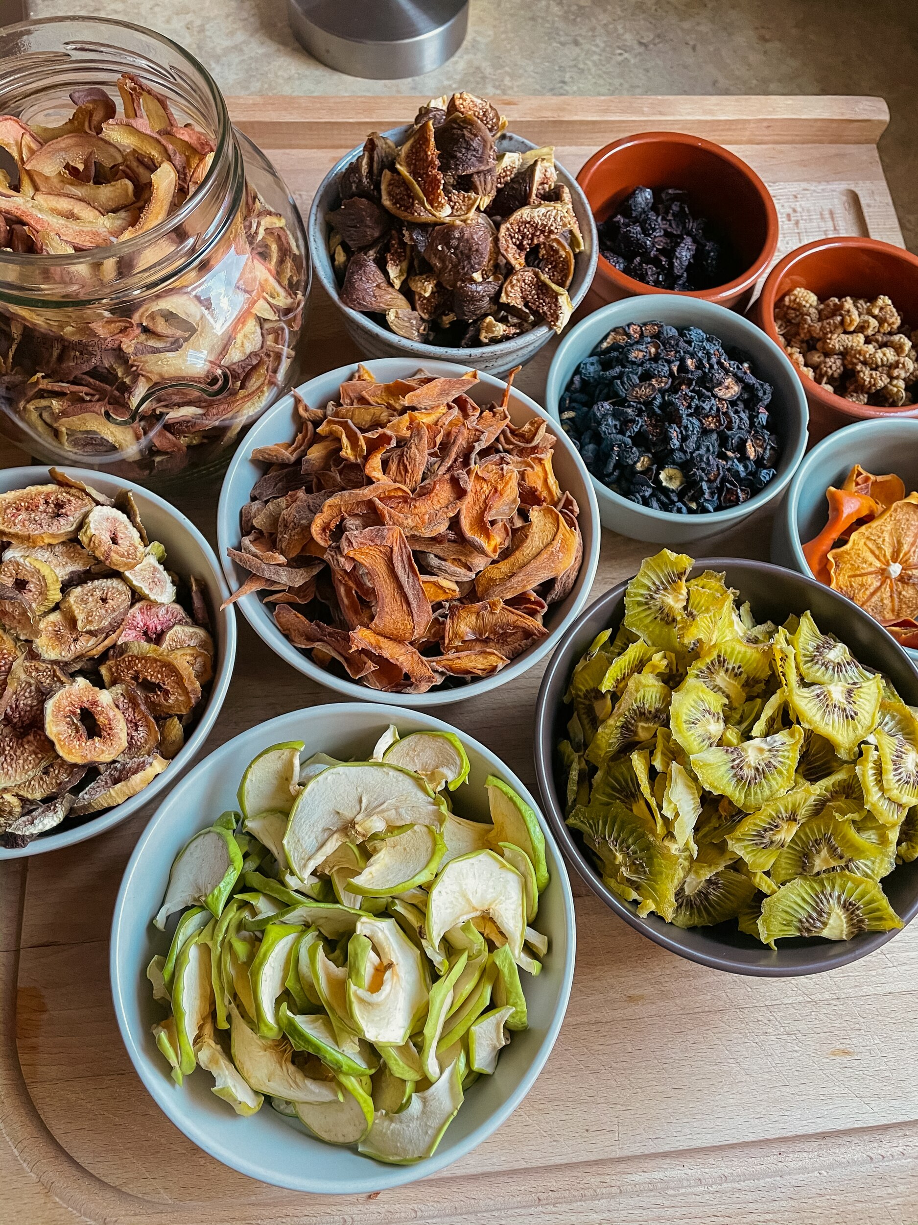 Blue bowls filled with dried apple slices, kiwi, figs and an assortment of other dried fruit