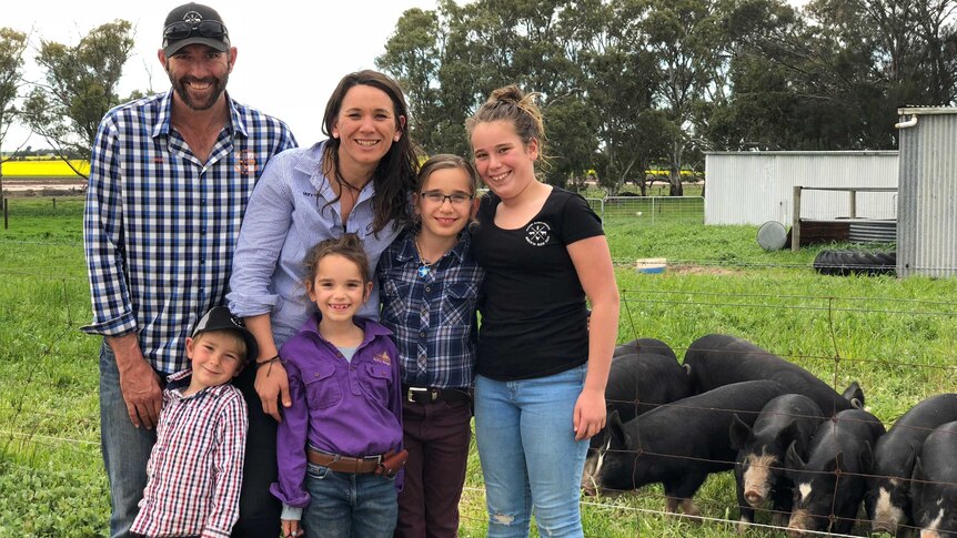 A farming family from Cummins stands in front of their pigs.