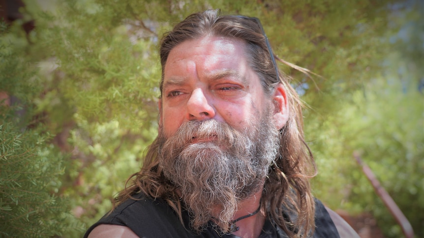 A man with an injured eye stands in front of a bush