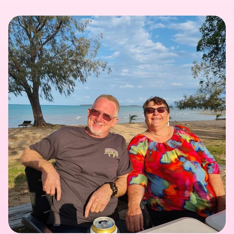 Un anciano y una anciana se sientan en la playa sonriendo.