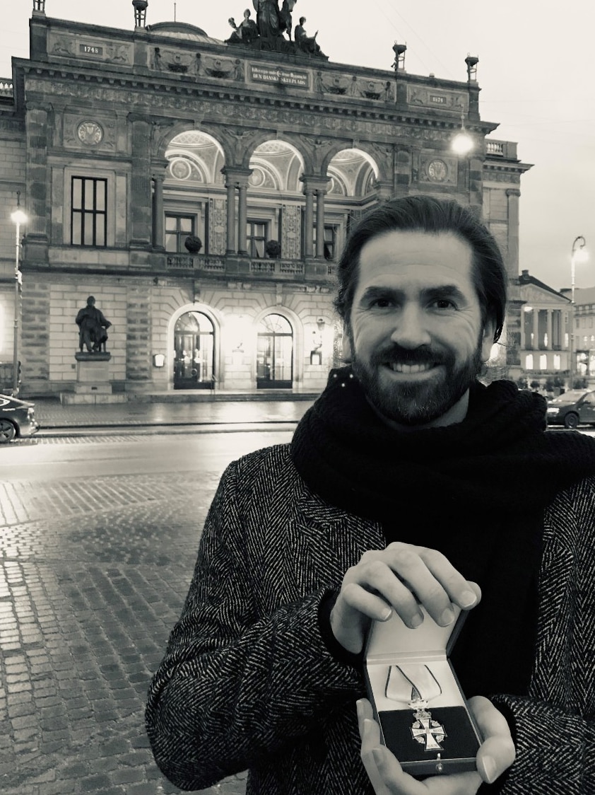 Former Toowoomba musician Steven Moore standing outside Copenhagen's Amalienborg Palace in a heavy jacket and scarf with award
