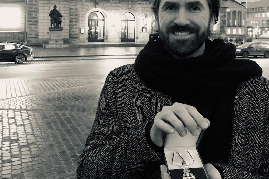 Former Toowoomba musician Steven Moore standing outside Copenhagen's Amalienborg Palace in a heavy jacket and scarf with award