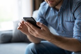 Close-up of a man sitting on a grey couch using his smartphone