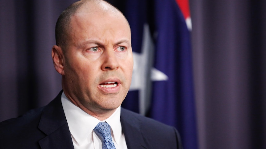 Josh Frydenberg in a suit and tie standing in front of a lecturn in a blue room in front of an australian flag