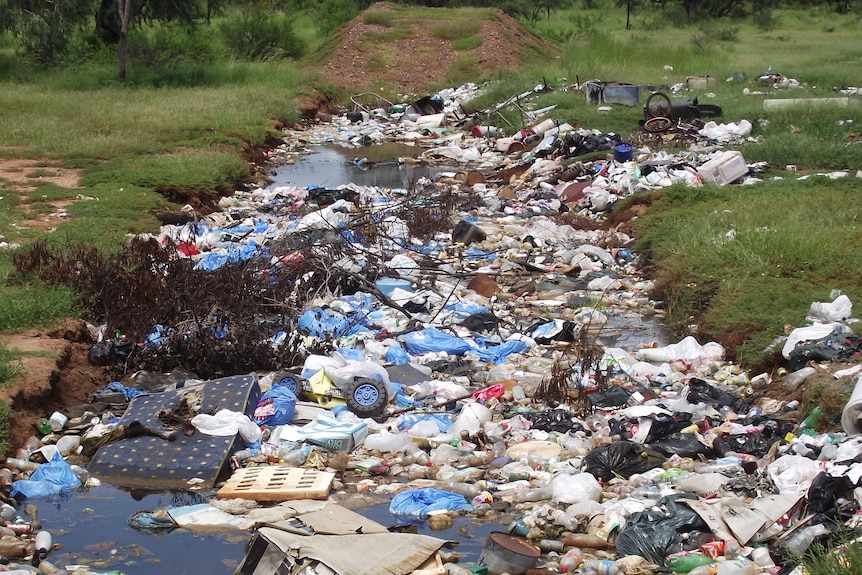 Trench full of water and rubbish with green grass either side