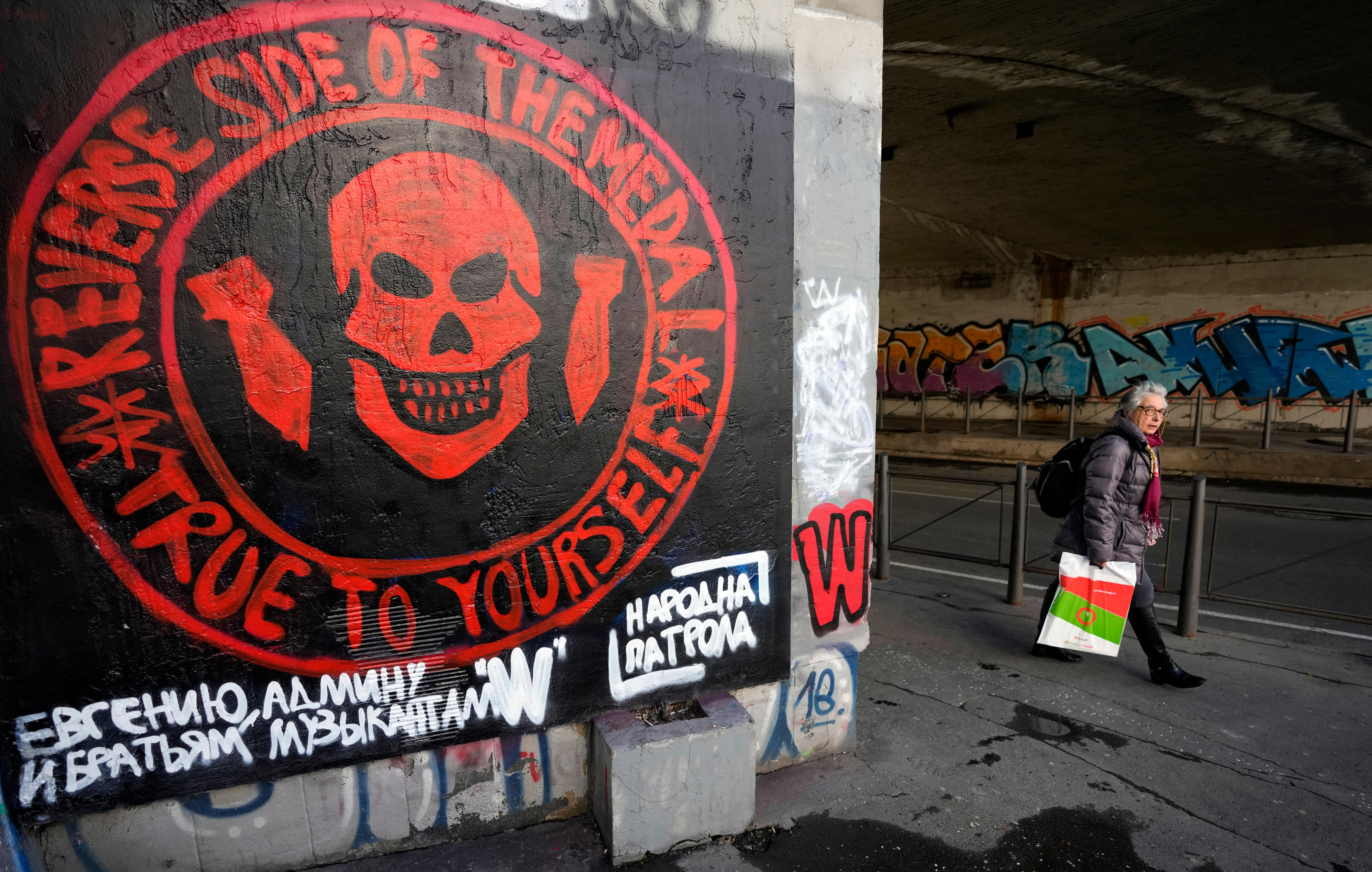 A woman walks past a wall painted in black with a red circular symbol on it. 