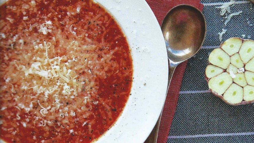 Roast tomato and garlic soup in a bowl alongside a garlic clove cut in half.