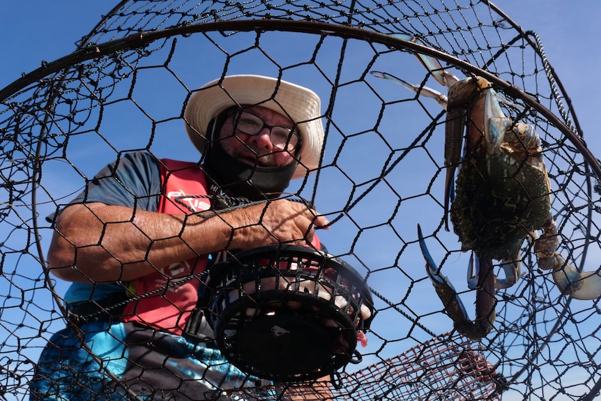 Bill Kearns in fishing attire holding a net with a crab inside. 