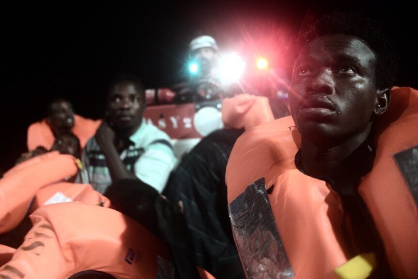 An asylum seeker man in a life vest looks up from a boat at night time after being rescued from the sea.