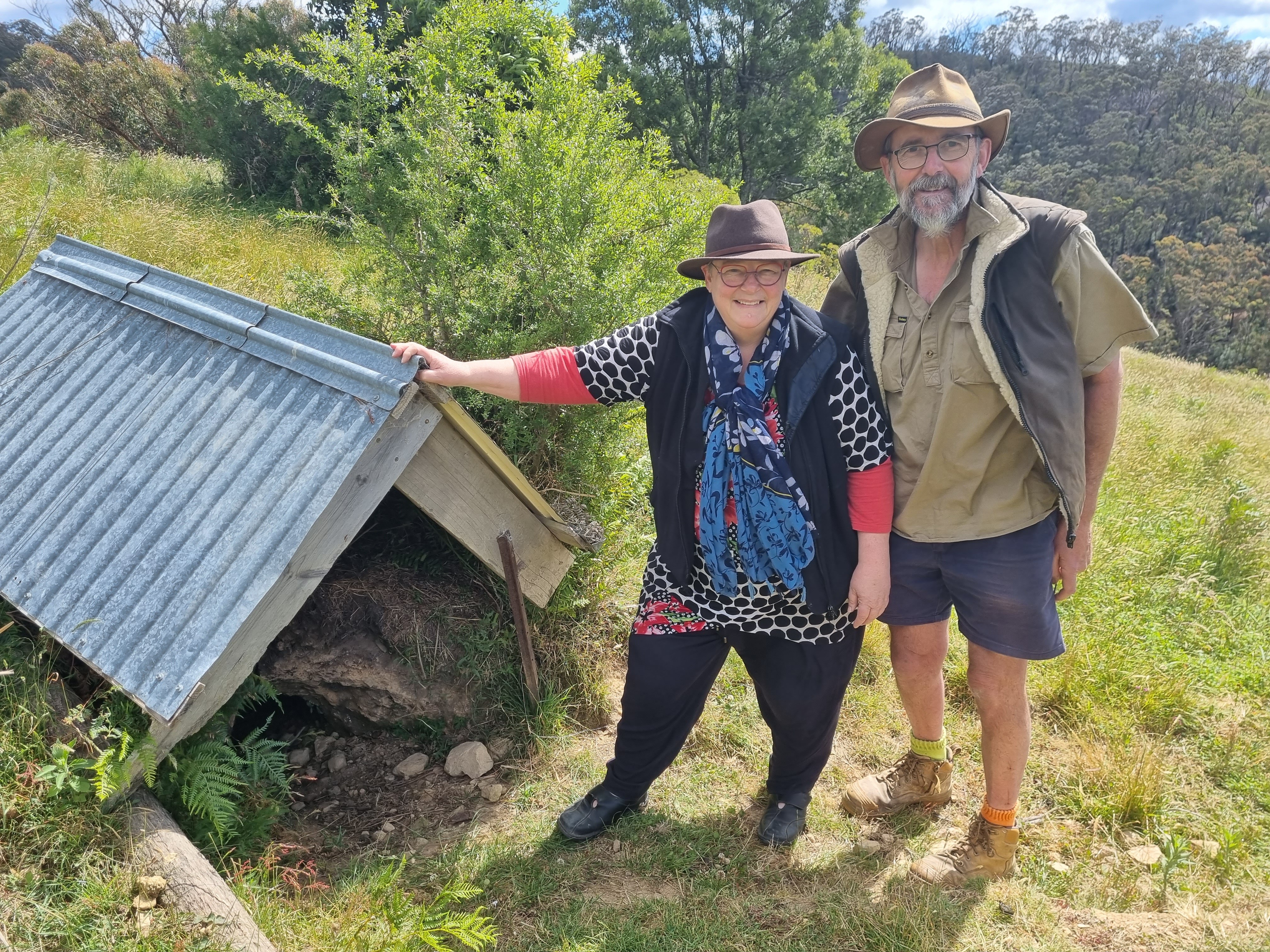 A man and a woman standing next to a shed over a hole