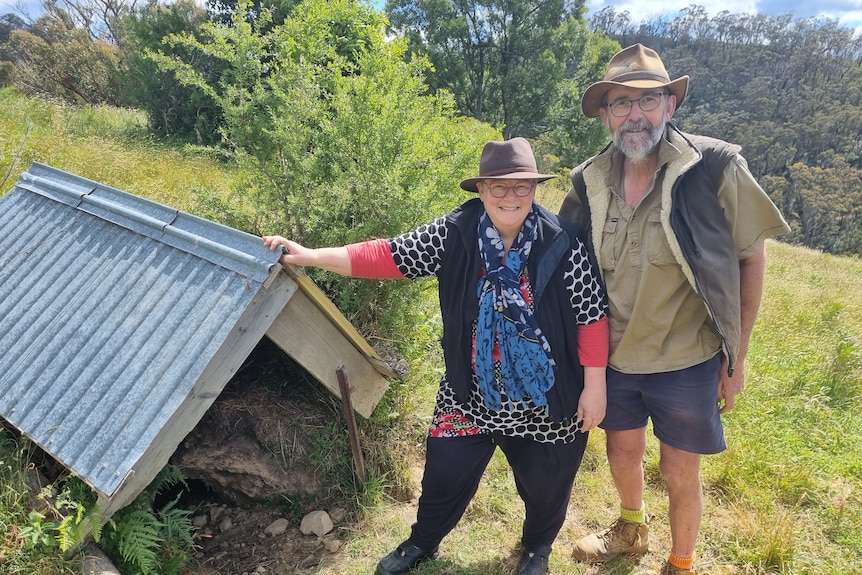 A man and a woman standing next to a shed over a hole 
