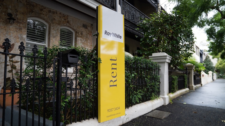 A "for rent" sign outside a terrace house on an empty wet street