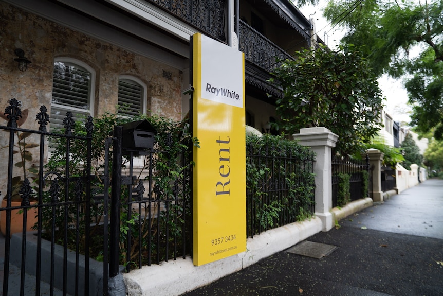 A "for rent" sign outside a terrace house on an empty wet street