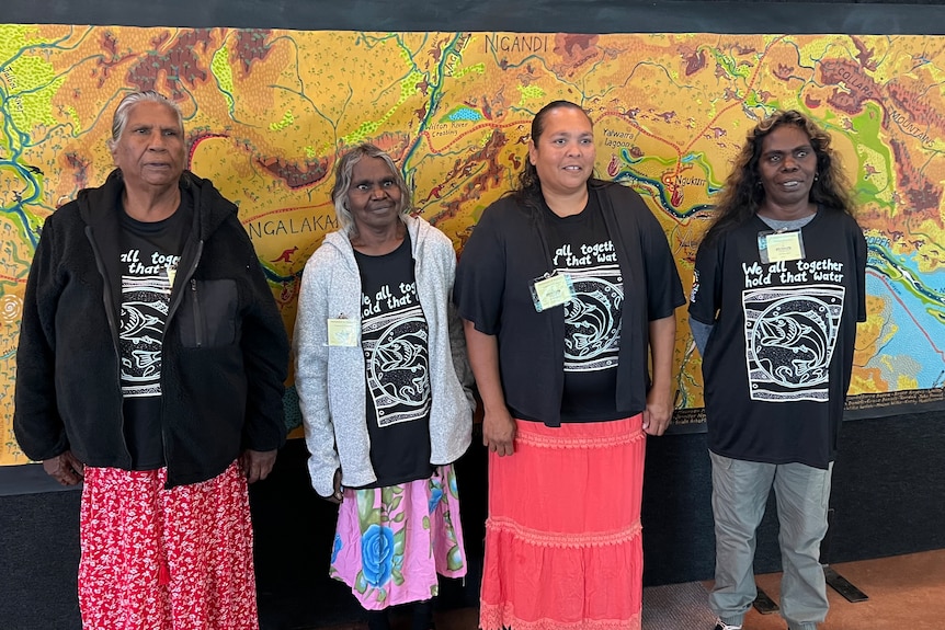 Four women stand in front of a large and colourful map.