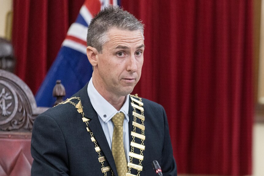 A man standing at a council meeting wearing his mayoral chains.  
