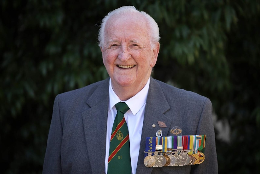 War veteran Matthew Rennie smiles as he wears his medals on the front of his suit.