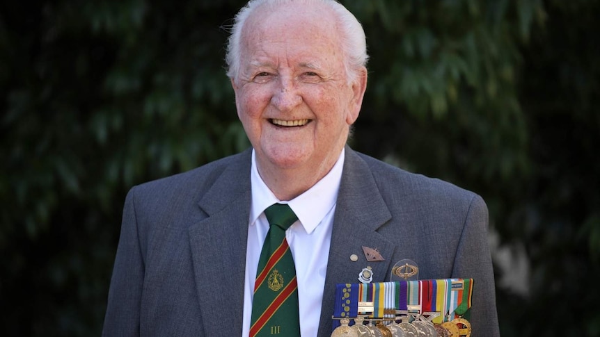 War veteran Matthew Rennie smiles as he wears his medals on the front of his suit.