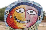 A large colourful mosaic sculpture of a smiling boy's face
