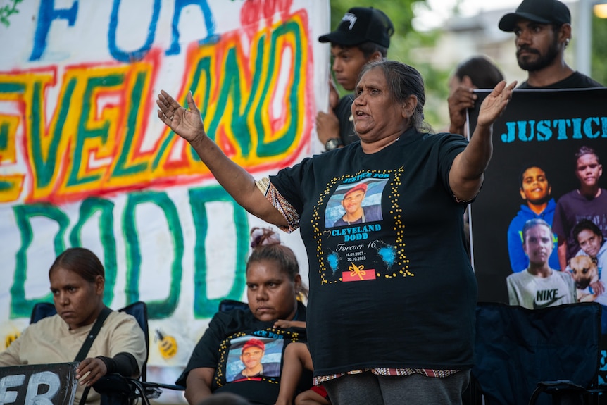 An older Indigenous lady raises up her arms as she addresses a rally calling for justice