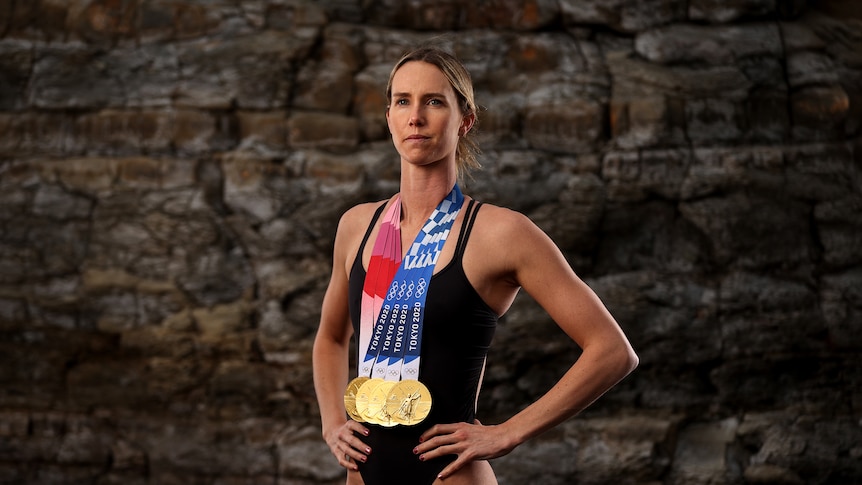 Emma McKeon poses in front of a rock wall with all her medals.