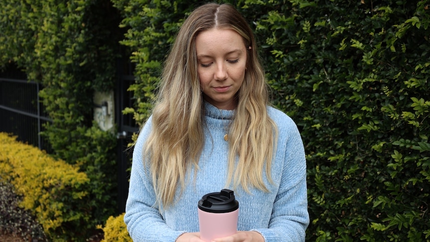 A woman wearing a blue jumper with blonde hair looking down at a pink coffee cup