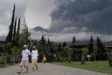People at a temple as Mt Agung volcano erupts in background.