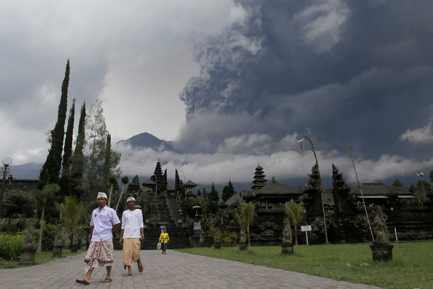 People at a temple as Mt Agung volcano erupts in background.