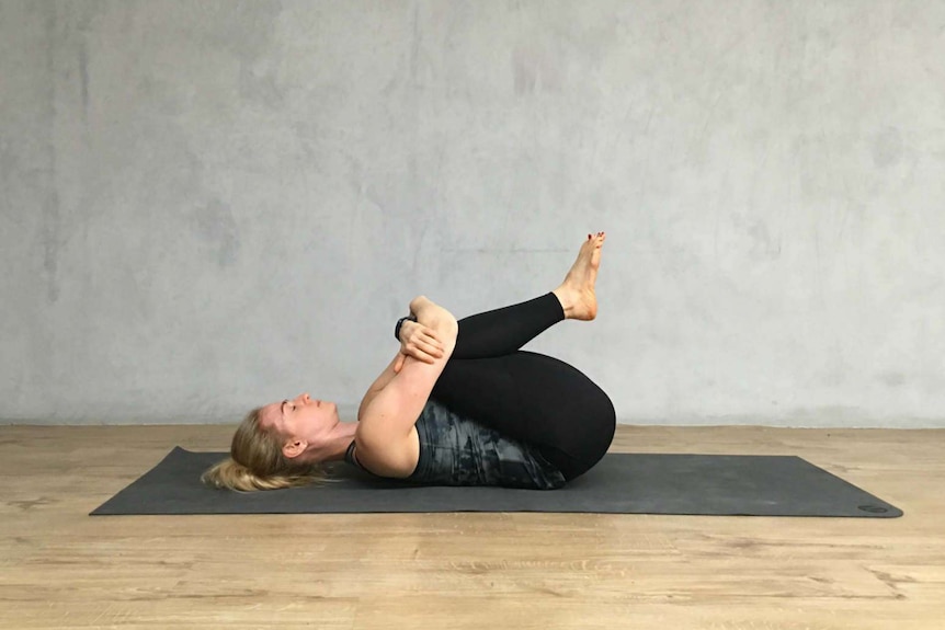 A yoga instructor demonstrates the knees to chest pose.