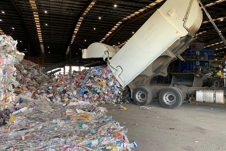 A rubbish truck tips tonnes of recycling into a pile in a warehouse.