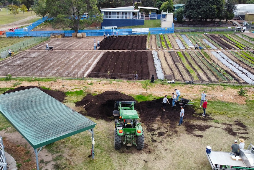 A drone photo of a farm near a school with a green tracker and rows of vegetables.