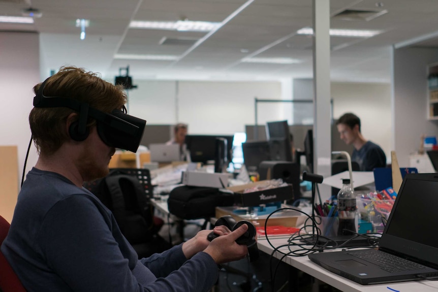 A student experiments with a virtual reality headset strapped to his head and two controllers.