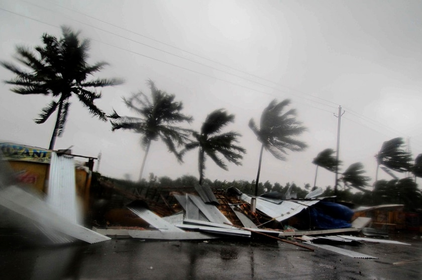 Shops have collapsed onto a street as palm trees are blown around in the strong winds of a cyclone