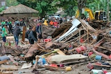 Locals sift through rubble and debris with a yellow crane seen in the background during tsunami clean-up.
