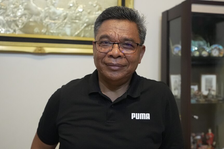 A man with black shirt and glasses, smiling, looking down the camera.