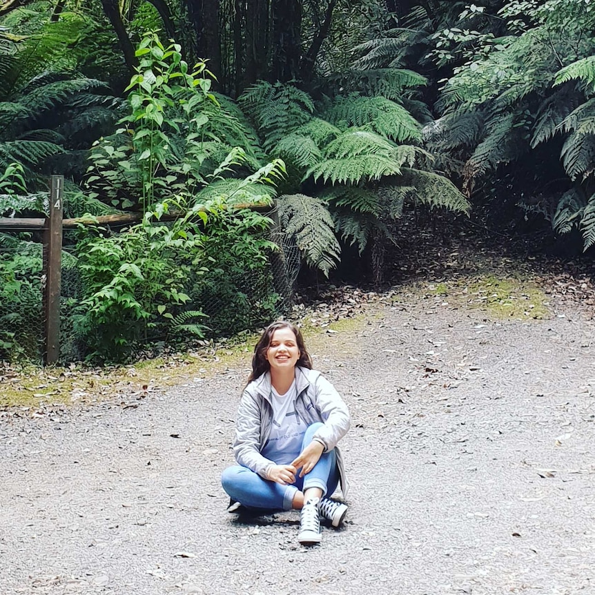 Young girl sitting on ground with nature around.