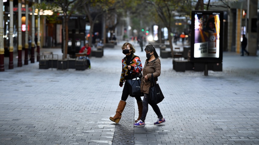 两个戴着口罩的女人走在空荡荡的购物区