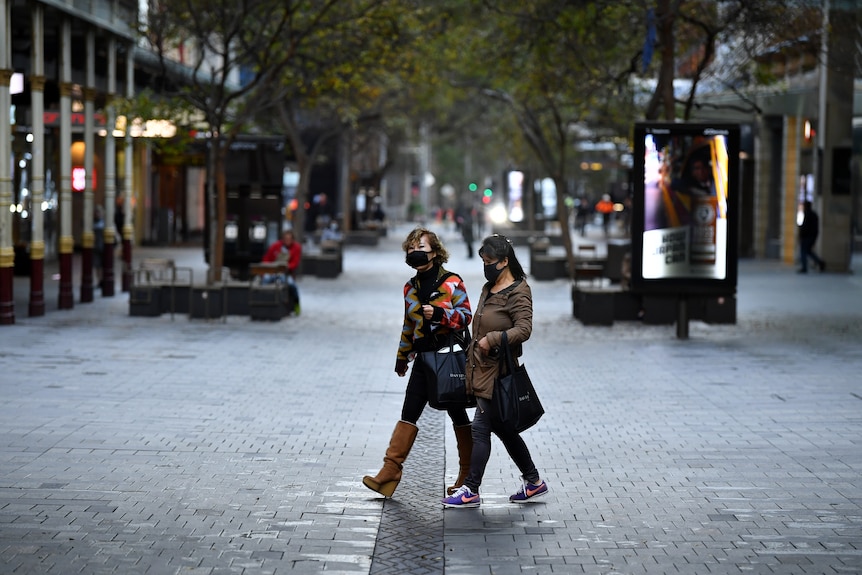 Two women wearing masks walk down an empty shopping strip