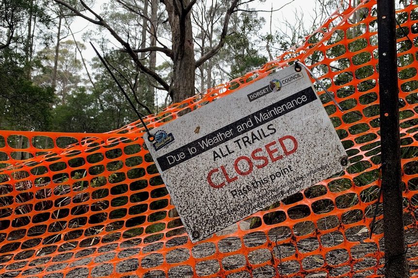 A mud-splattered 'closed' sign hanging on orange plastic tape