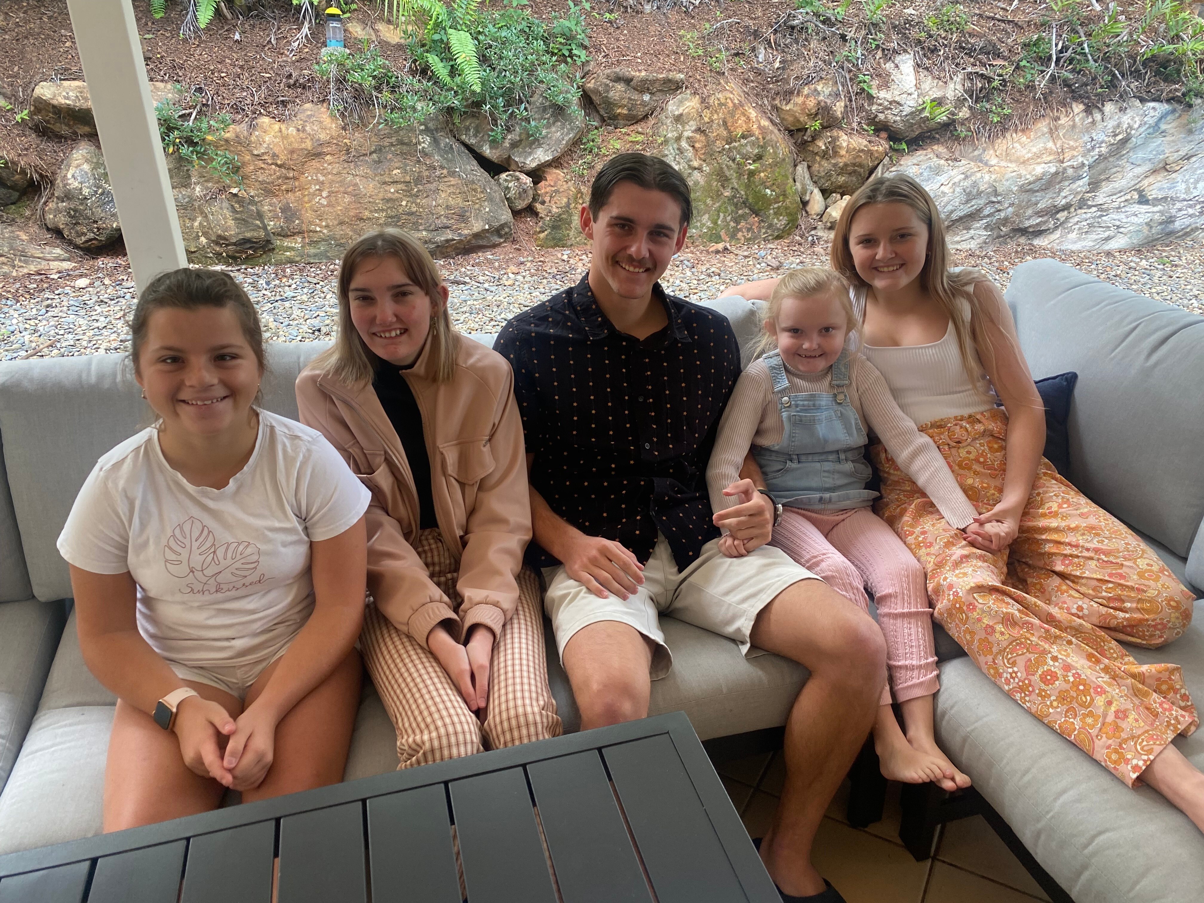 Five children of various ages sit on a couch. 