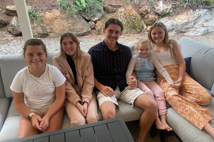 Five children of various ages sit on a couch. 