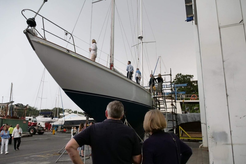 People walk on the yacht which is lifted out of the water on the dock.