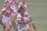 A woman charges past defenders in driving rain during a rugby league match