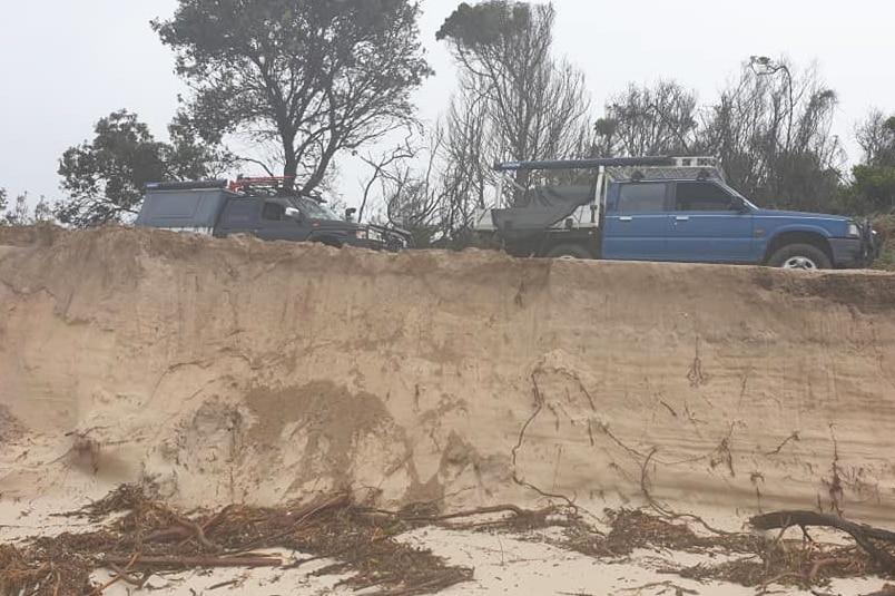 Two four-wheel-drive vehicles parked on top of an eroded beach bank at Woorim Beach.