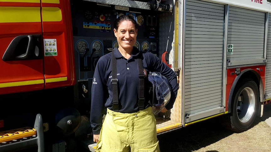 Kate Oliver holds her helmet in front of a fire truck