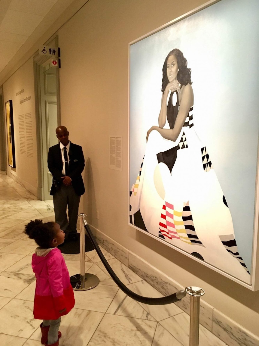 Parker Curry staring up with her mouth open at a painting of Michelle Obama