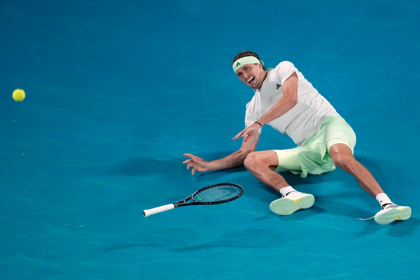 Alex Zverev on the ground after dropping his racquet as a tennis ball flies away at the Australian Open.