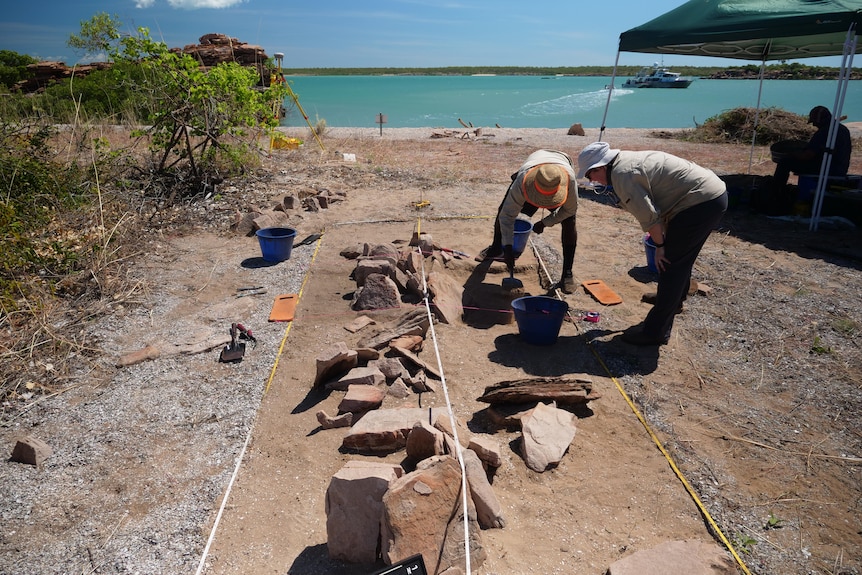 Two people standing and looking at an archaeological dig site on a beach.